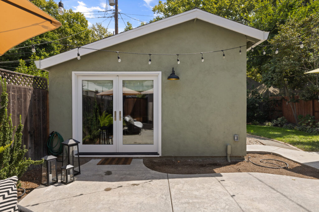 garage conversion Sacramento completed ADU: modern green stucco exterior with French doors, string lights, patio, and landscaping in Land Park

